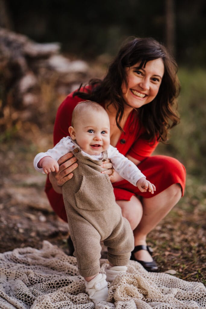 Family Photographer, a mother holds her baby, both smiling as practices walking outside